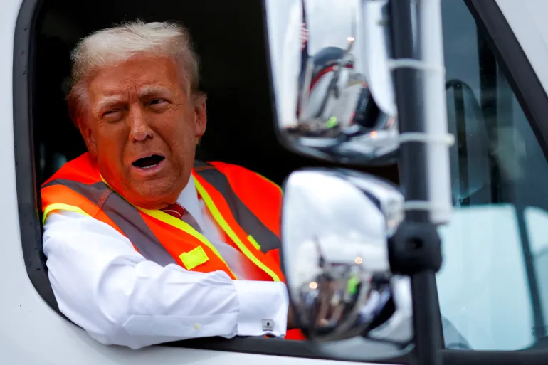 President Donald Trump reacts as he sits in a garbage truck