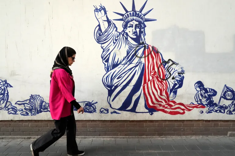 A woman walks past an anti-American mural on the wall of the former US Embassy in Tehran, Iran, Saturday, August 19